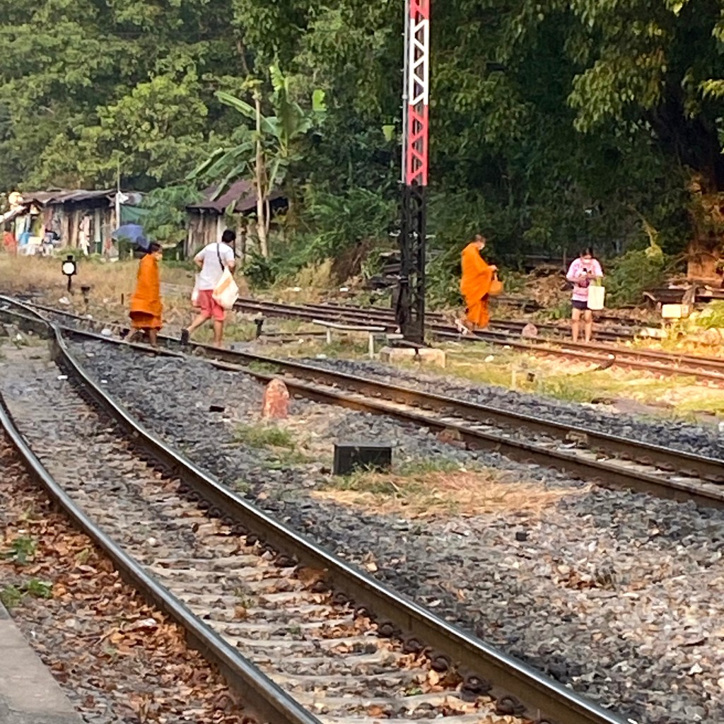 Monks in their orange robes and people walking across the railway track at Thonburi railway station