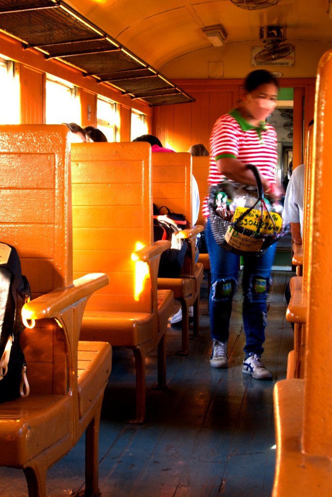A woman walking through the train carriage selling snacks and drinks to passengers